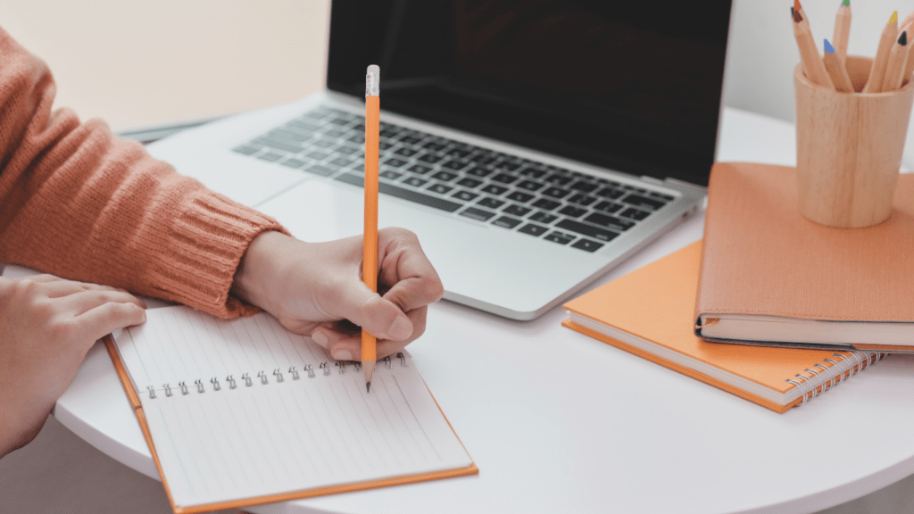 a person is sitting at a table with a notebook and pencil