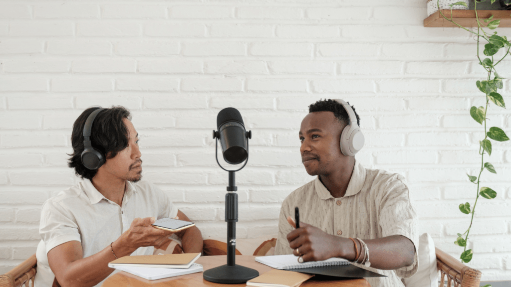 two people sitting at a table with a microphone and notebook