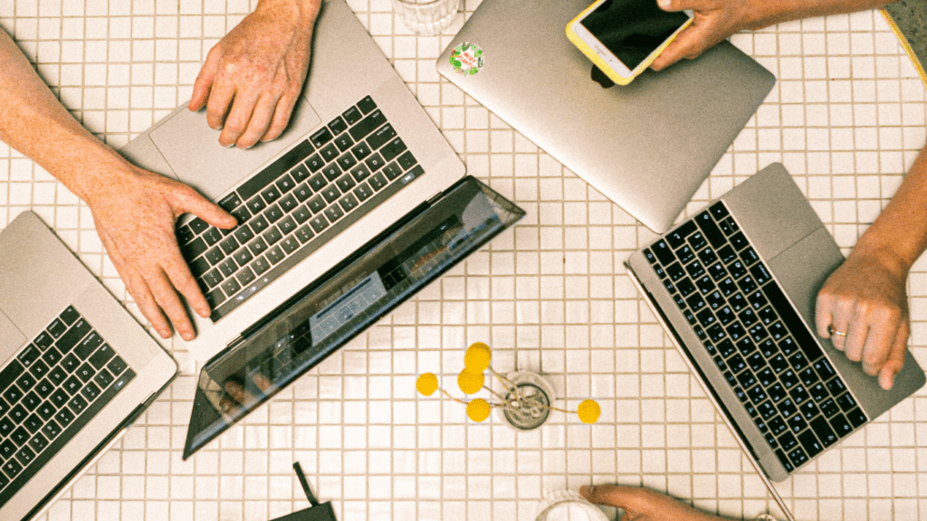 a group of people sitting around a table with laptops and papers