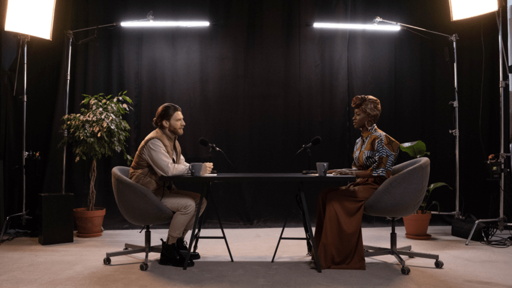 two people sitting at a table with a microphone and notebook